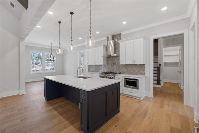 kitchen featuring visible vents, light wood-style floors, white cabinetry, a sink, and wall chimney exhaust hood