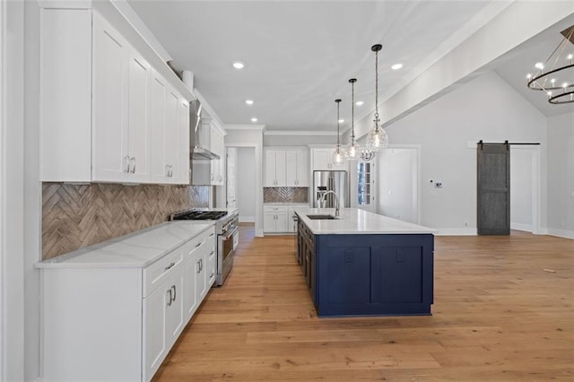 kitchen with a barn door, tasteful backsplash, white cabinets, stainless steel appliances, and a sink