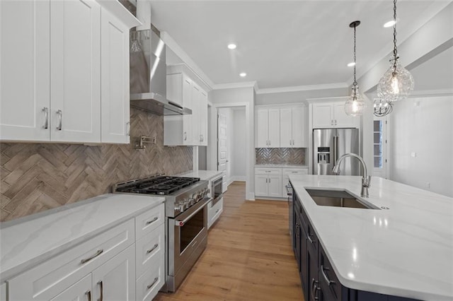 kitchen featuring wall chimney exhaust hood, appliances with stainless steel finishes, hanging light fixtures, white cabinetry, and a sink