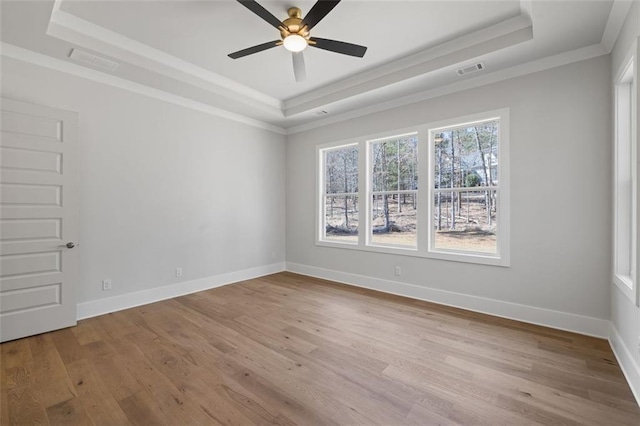 empty room with wood finished floors, a raised ceiling, and visible vents