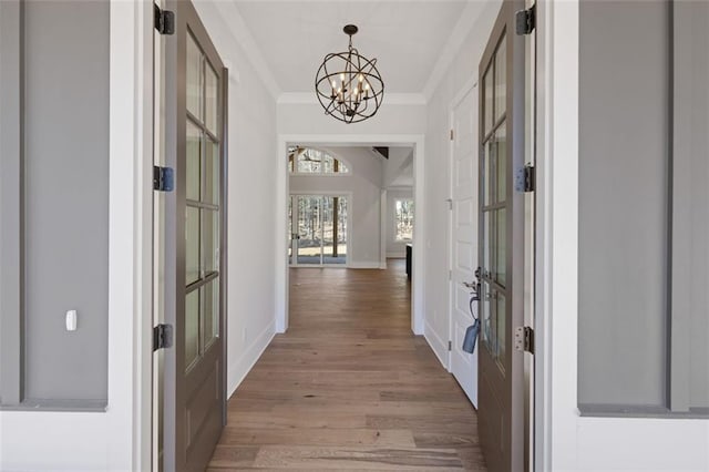 hallway with a notable chandelier, ornamental molding, wood finished floors, and baseboards