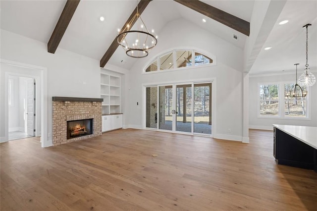 unfurnished living room with built in shelves, a notable chandelier, light wood-style flooring, and beamed ceiling