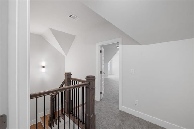 hall featuring carpet floors, lofted ceiling, visible vents, an upstairs landing, and baseboards