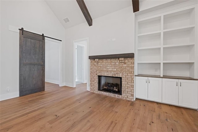 unfurnished living room featuring visible vents, a barn door, light wood-style floors, a brick fireplace, and beamed ceiling