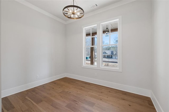 empty room featuring visible vents, baseboards, ornamental molding, wood finished floors, and a notable chandelier