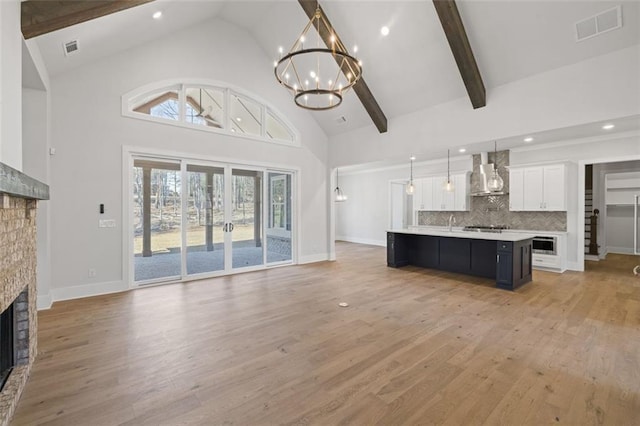 kitchen with a fireplace, light countertops, visible vents, an inviting chandelier, and wall chimney range hood