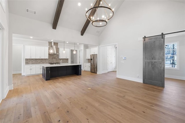 kitchen with a barn door, visible vents, stainless steel fridge with ice dispenser, wall chimney exhaust hood, and open floor plan