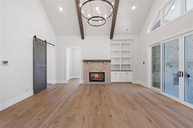 unfurnished living room with a fireplace, light wood finished floors, a barn door, beamed ceiling, and baseboards