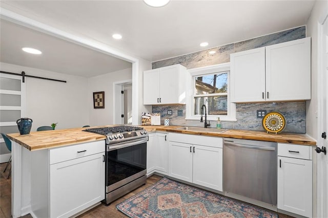 kitchen with sink, white cabinetry, stainless steel appliances, wood counters, and a barn door