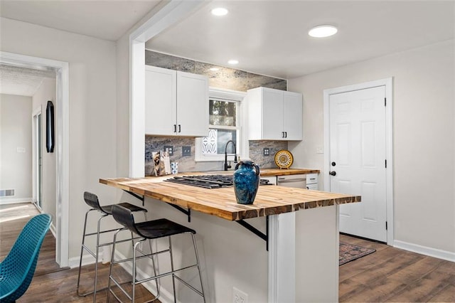 kitchen with a breakfast bar area, butcher block counters, backsplash, white cabinetry, and dark hardwood / wood-style flooring