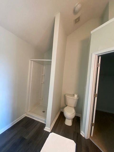 bathroom featuring walk in shower, toilet, hardwood / wood-style floors, and vaulted ceiling