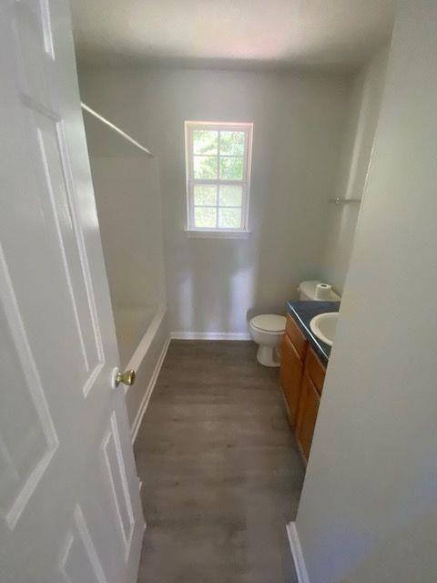 bathroom with walk in shower, vanity, toilet, and wood-type flooring