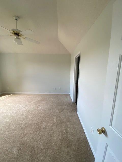 carpeted spare room featuring ceiling fan and vaulted ceiling