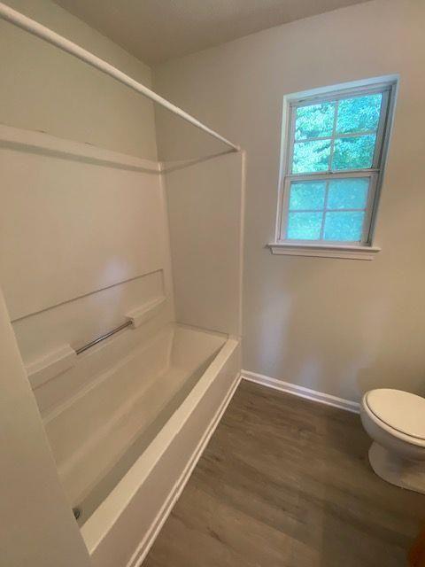 bathroom with washtub / shower combination, toilet, and hardwood / wood-style floors