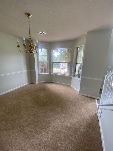 unfurnished dining area featuring plenty of natural light, carpet flooring, and a notable chandelier