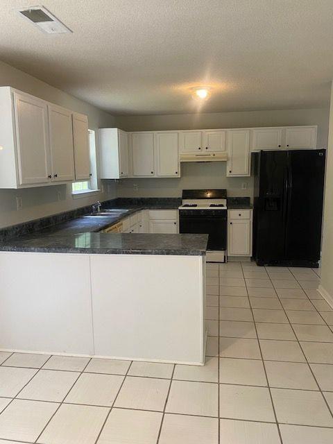 kitchen featuring black fridge with ice dispenser, a textured ceiling, white range with gas cooktop, kitchen peninsula, and white cabinets