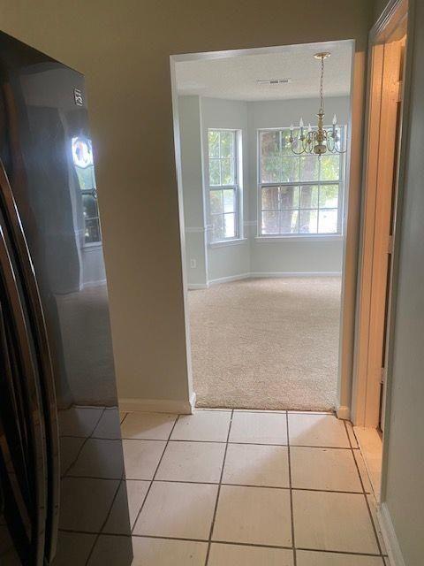 hallway with light tile patterned flooring and a notable chandelier