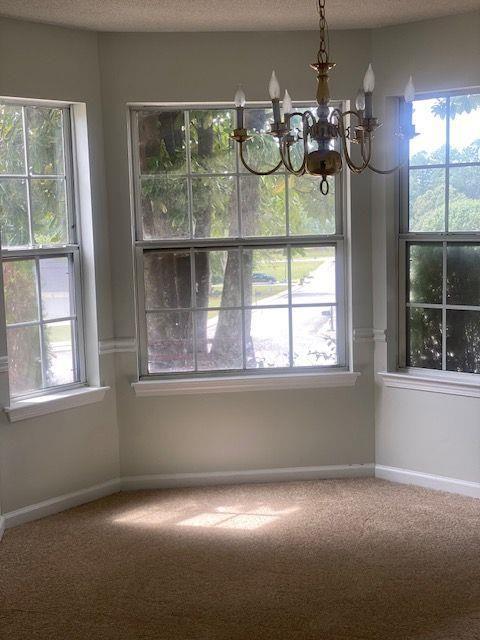 unfurnished dining area with plenty of natural light, carpet flooring, a chandelier, and a textured ceiling