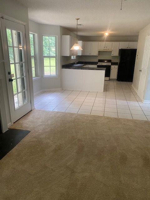 kitchen featuring hanging light fixtures, stainless steel range with electric cooktop, white cabinets, black fridge, and light colored carpet