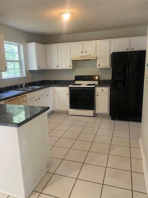 kitchen featuring sink, black fridge, light tile patterned floors, white range with gas cooktop, and white cabinets