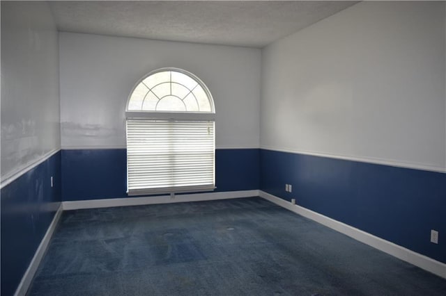 spare room featuring a textured ceiling and dark colored carpet