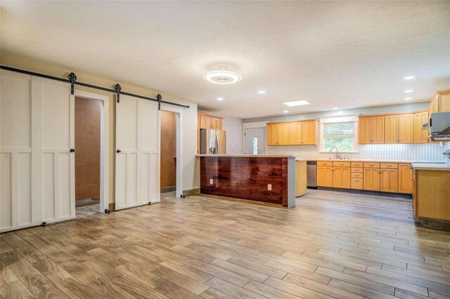 kitchen with appliances with stainless steel finishes, a barn door, light hardwood / wood-style floors, and sink