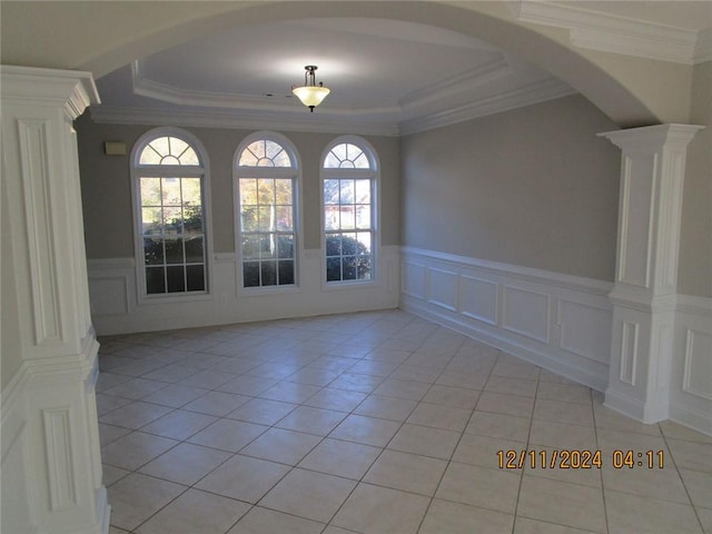 empty room with light tile patterned floors, decorative columns, arched walkways, and a decorative wall