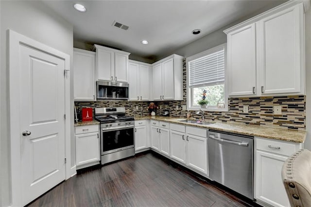 kitchen with light stone countertops, stainless steel appliances, white cabinets, sink, and dark hardwood / wood-style flooring