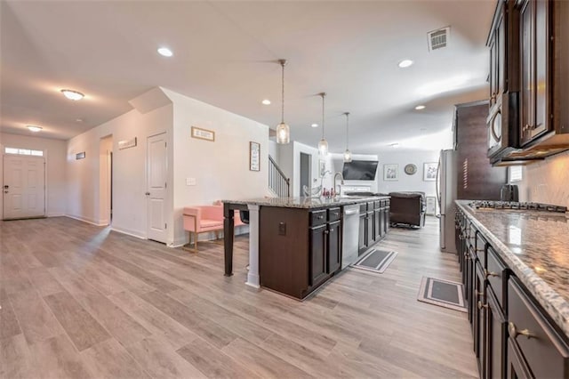 kitchen with stainless steel appliances, dark brown cabinetry, an island with sink, a kitchen bar, and decorative light fixtures