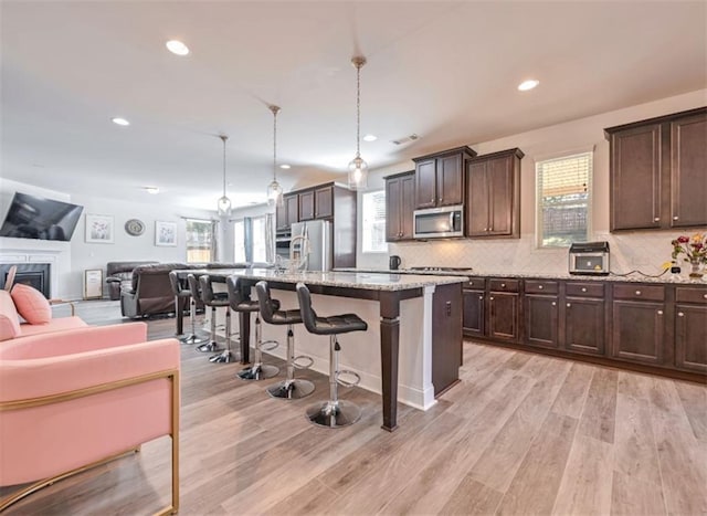 kitchen with pendant lighting, a breakfast bar, appliances with stainless steel finishes, light stone countertops, and a center island with sink