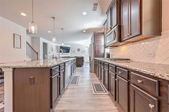 kitchen with appliances with stainless steel finishes, tasteful backsplash, hanging light fixtures, a kitchen island with sink, and dark brown cabinets