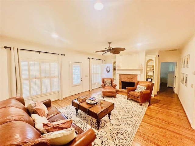 living room with light wood-type flooring, ceiling fan, and a fireplace