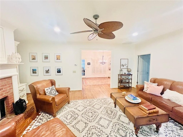 living room featuring ceiling fan with notable chandelier, a brick fireplace, and light wood-type flooring