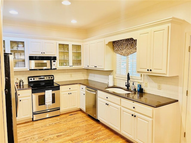 kitchen with appliances with stainless steel finishes, backsplash, light wood-type flooring, ornamental molding, and sink