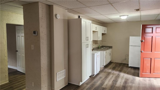 kitchen featuring sink, white refrigerator, dark hardwood / wood-style flooring, white cabinets, and a drop ceiling