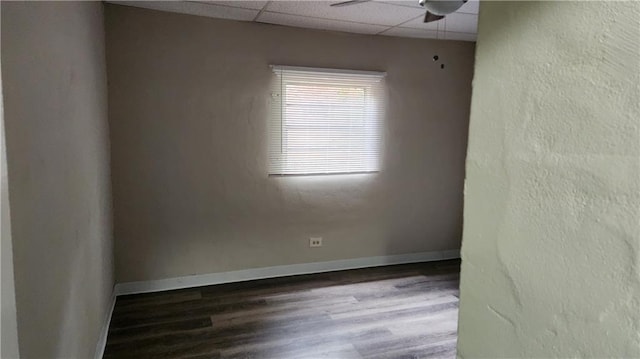 empty room with ceiling fan, a paneled ceiling, and dark wood-type flooring