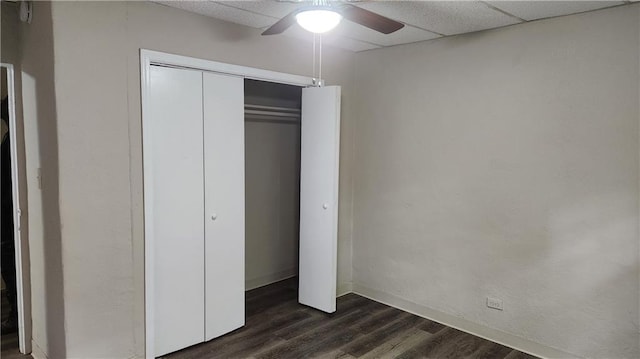 unfurnished bedroom with dark hardwood / wood-style flooring, a paneled ceiling, ceiling fan, and a closet