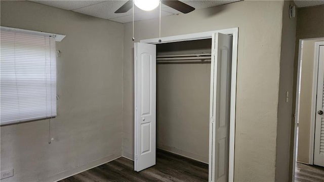 unfurnished bedroom featuring dark wood-type flooring, a closet, ceiling fan, and a paneled ceiling