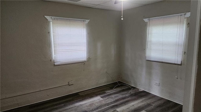 spare room with a drop ceiling and dark hardwood / wood-style flooring