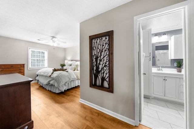 bedroom featuring light wood-style flooring, a ceiling fan, a sink, ensuite bath, and baseboards