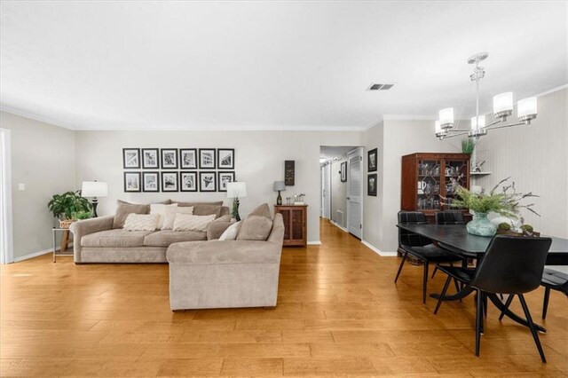 living area featuring a chandelier, ornamental molding, light wood finished floors, and baseboards