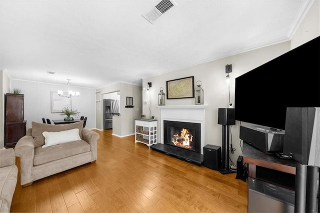 living room featuring ornamental molding, a glass covered fireplace, visible vents, and wood finished floors