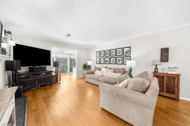 living room with visible vents, light wood-style floors, ornamental molding, and a ceiling fan