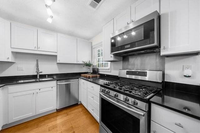 kitchen with stainless steel appliances, a sink, dark countertops, white cabinetry, and a textured ceiling