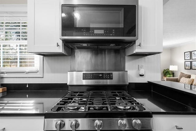 kitchen with white cabinetry, appliances with stainless steel finishes, decorative backsplash, dark countertops, and crown molding