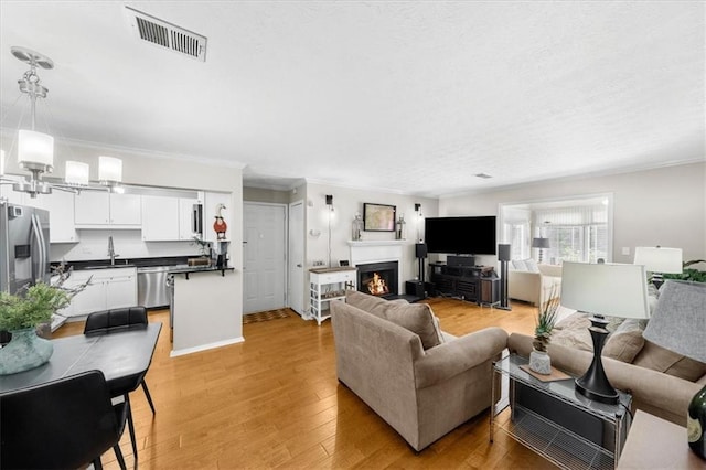 living room featuring a warm lit fireplace, crown molding, visible vents, and light wood-style floors