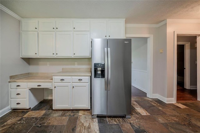 kitchen with stone tile floors, baseboards, stainless steel fridge, and white cabinets