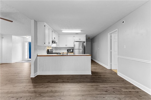 kitchen with stainless steel appliances, a peninsula, a textured ceiling, dark wood finished floors, and under cabinet range hood