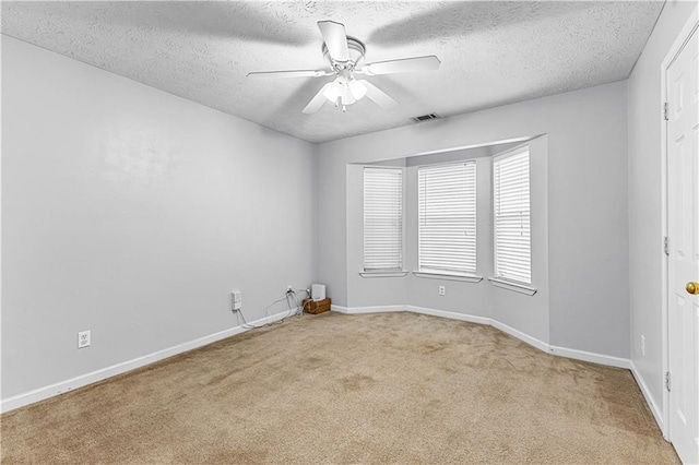 carpeted empty room with baseboards, a ceiling fan, a textured ceiling, and visible vents