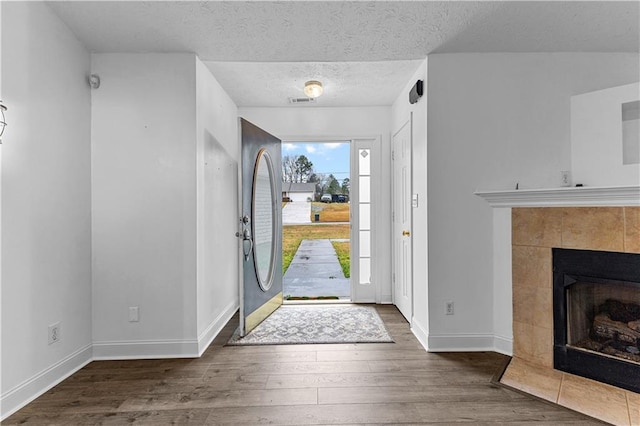 entryway with baseboards, wood finished floors, a textured ceiling, and a tiled fireplace